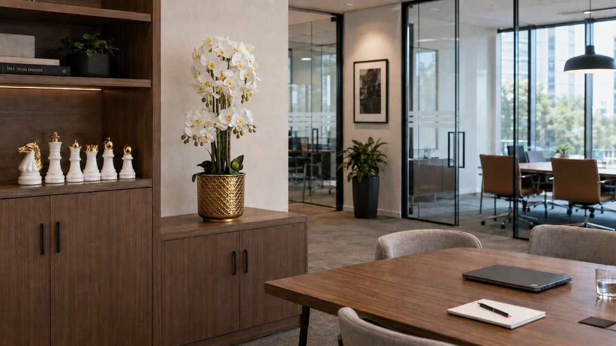 White orchid arrangement in a gold planter beside white and gold chess ornaments in a contemporary office