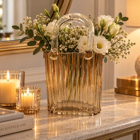 Amber ribbed glass handbag vase filled with white flowers beside candles on a console