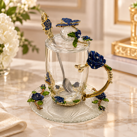 Glass tea cup and saucer set with metal blue roses and a blue butterfly, lid and spoon, on a marble table