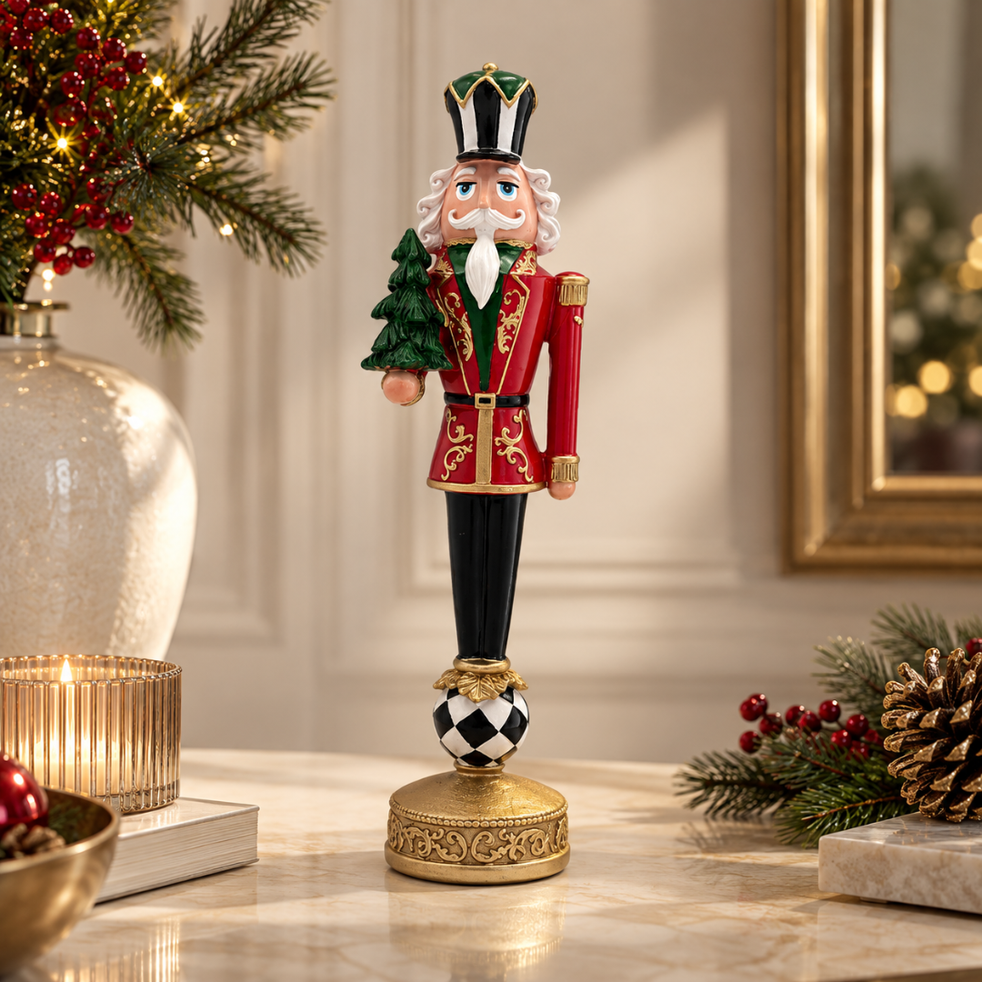 A decorative Christmas nutcracker figurine stands on a marble tabletop in a warmly lit holiday setting. The nutcracker wears a red coat with gold trim, black pants, and a green-and-white striped hat, while holding a small green tree.